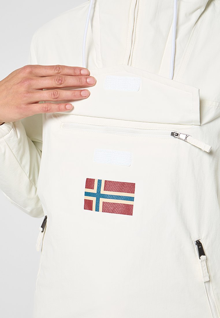 Person hebt einen Klappverschluss an einer weißen Jacke mit norwegischem Flaggenpatch, sichtbaren vorderen Reißverschlusstaschen und Kordelzügen an.