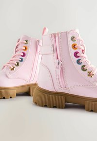 Stivali alla caviglia in pelle lucida rosa con suola in gomma texture, lacci anteriori e cerniere, caratterizzati da occhiali multicolori e dettagli a stella.