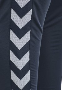 Svarta sportleggings med ett strukturerat silverfärgat chevronmönster längs sidan, tillverkade av stretchigt och andningsbart material.