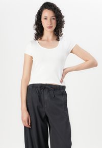 White short-sleeve top with a scoop neckline, paired with black drawstring pants featuring side pockets and textured accents.