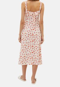 Blumen-Midi-Kleid mit einem hellbeigen Hintergrund, Rüschen-Trägern und einer Bindung im Rücken. Es zeigt überall kleine rote und pinke Blumen.
