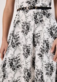 Vestido con estampado floral en blanco y negro, hecho de un tejido ligero, que presenta un corsé ajustado, una falda acampanada y un cinturón negro con detalles dorados.