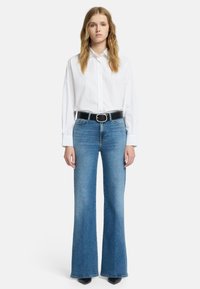 Biała koszula na guziki w połączeniu z jasnoniebieskimi rozszerzanymi dżinsami i czarnym paskiem z okrągłą srebrną klamrą. Smukły i dopasowany fason.