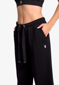 Pantaloni sportivi negri dintr-un material moale, cu talie elastică, închidere cu șnur, buzunare laterale și un accent cu logo alb.