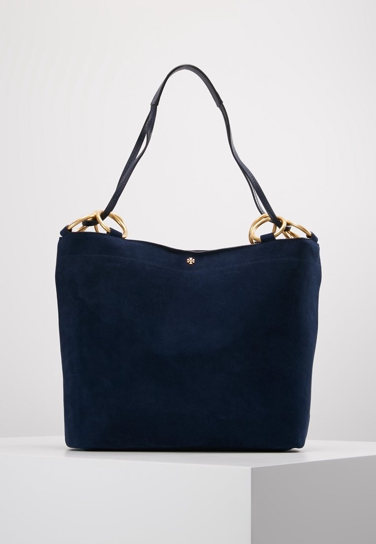 Sac à main en daim bleu marine avec une unique bandoulière en cuir noir et des anneaux métalliques dorés sur les bords supérieurs.
