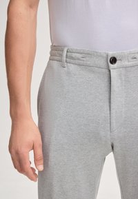 Helle graue Sweatpants mit strukturiertem Finish, flacher Vorderseite, Taillenbund mit Falten und einem einzelnen Knopfverschluss.