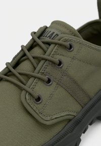 Παπούτσι από καμβά σε ελιά πράσινο με στρογγυλά μαύρα ρούχια, κορδόνια στο ίδιο χρώμα και υφασμένο λαστιχένιο πέλμα με ενισχυμένη μύτη.