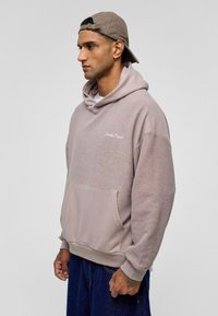 Verloofd-mauve hoodie met een gestructureerd oppervlak, grote voorkant zak en witte logo-stiksel. Lange mouwen en ribgebreide hem.