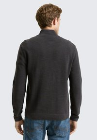Dunkelgrauer strukturierter Pullover mit hohem Kragen und gerippten Bündchen, kombiniert mit blauen Jeans. Minimalistisches Design, taillierte Passform.