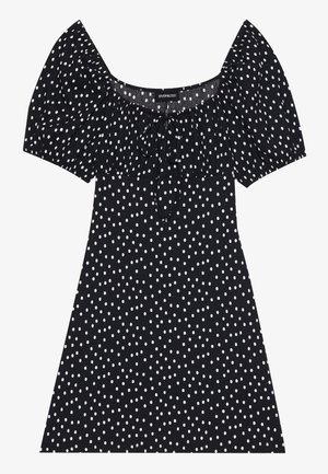 Svart kort kjole med hvite uregelmessige prikkede mønster, puffede ermer, firkantet halslinje og knyting foran.