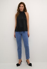 Black halter top with a gathered neck, paired with light blue skinny jeans and black high-heeled shoes featuring floral accents.