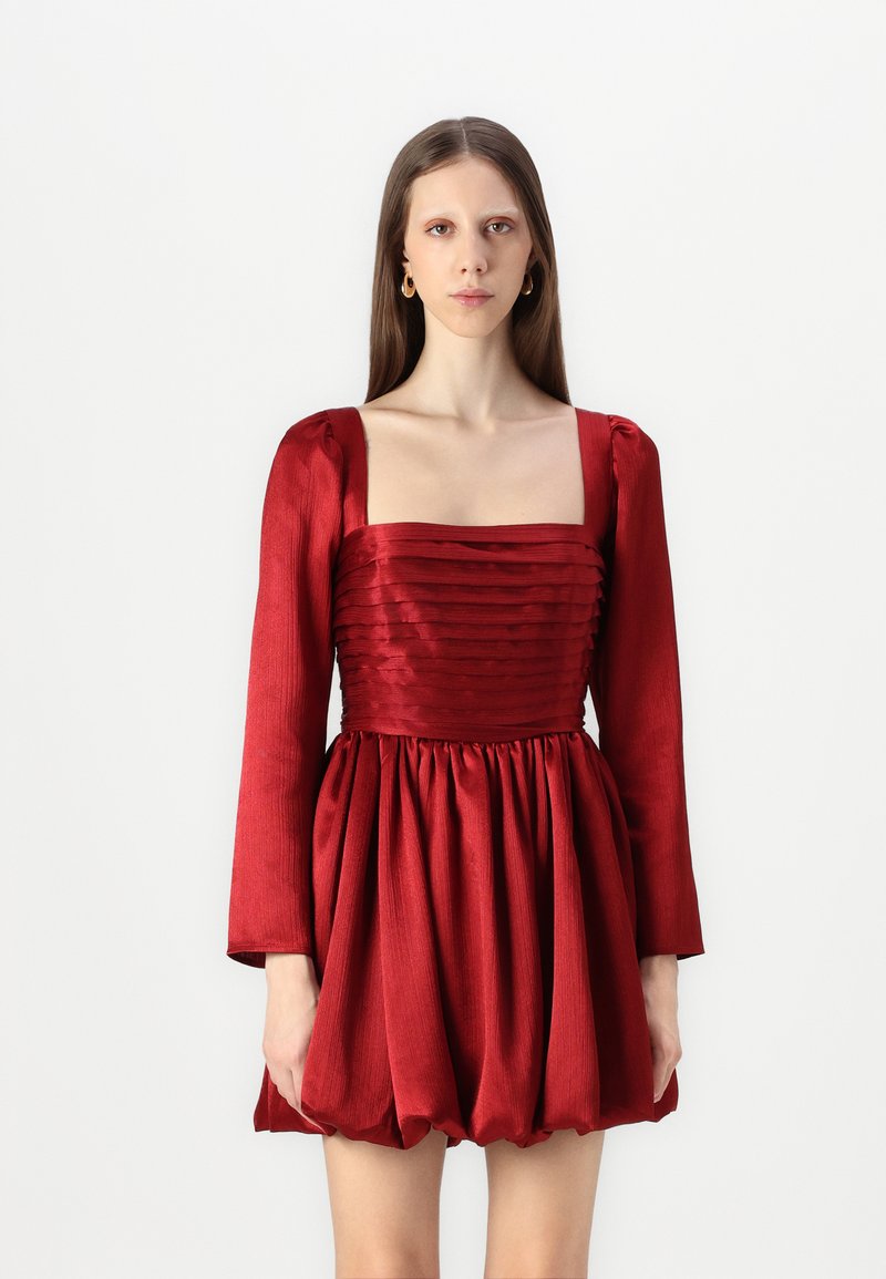 Rochie roșie din satin cu decolteu pătrat, corp plisat, mâneci lungi și fusta voluminoasă. Textură fină cu un luciu subtil.