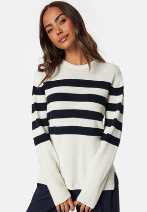 Pull rayé en crème et marine. Texture côtelée, col rond, manches longues et fentes sur les côtés à l'ourlet pour plus de confort.