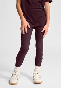 Bordeauxrote Leggings mit engem Schnitt und einem dezenten Zickzackmuster an der Seite. Kombiniert mit einem locker sitzenden dunklen Oberteil und weißen Sneakers.