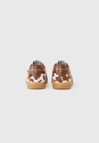 Sneaker marroni e bianchi con macchie, suola in gomma, tomaia in ecopelle e branding sulla linguetta del tallone. Design classico a bassa punta.