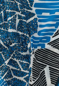 Κοντινή λήψη υφάσματος με γεωμετρικά και αφηρημένα σχέδια σε μπλε, μαύρο και λευκό, που περιλαμβάνουν τολμηρές ρίγες και ακανόνιστα σχήματα.