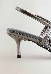 Metallisch zilveren hoge hak sandaal met een slanke hak, zwarte gestructureerde binnenzool en decoratieve pailletten op de band voor extra detail.