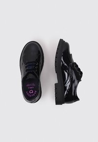 Zapatos de charol negro con punta redonda, detalles texturizados en los lados y una suela gruesa y resistente. El interior presenta una marca en color rosa.