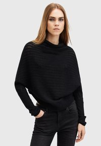 Maglione nero a vestibilità ampia con colletto a lupetto, caratterizzato da un design a maglia testurizzata e maniche lunghe. Abbinato a jeans neri.