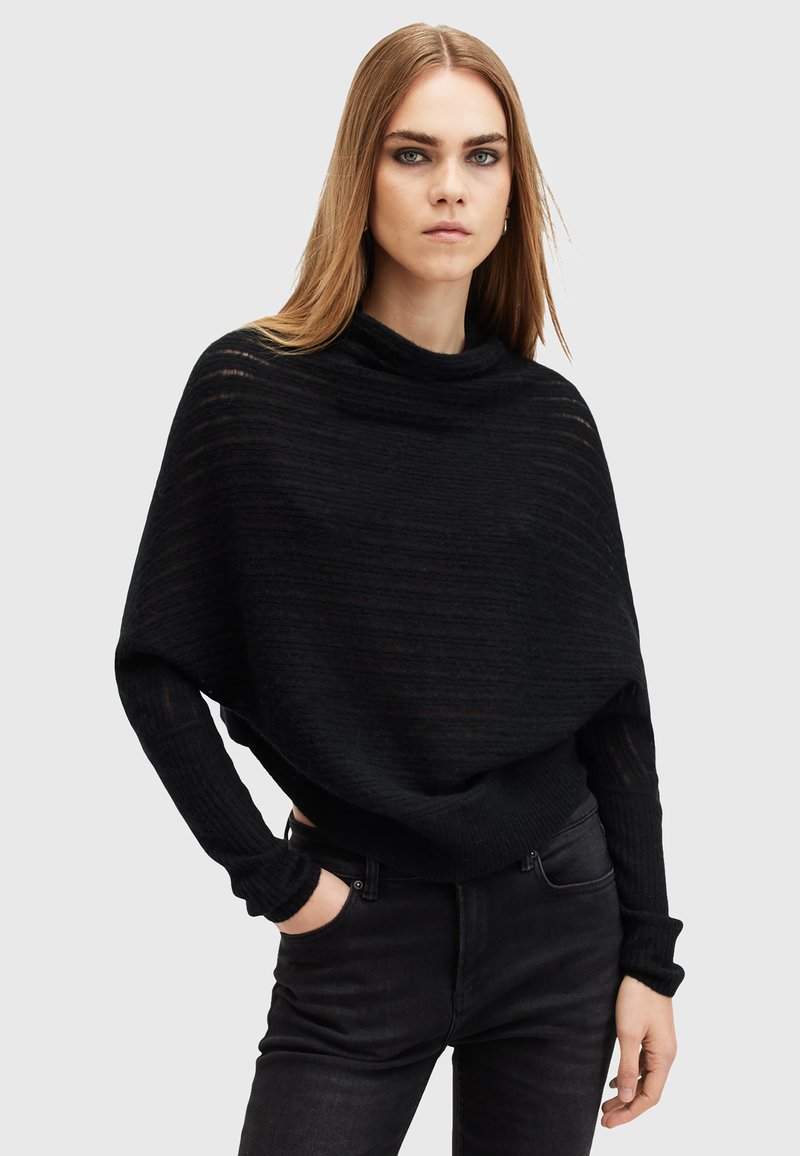 Maglione nero a vestibilità ampia con colletto a lupetto, caratterizzato da un design a maglia testurizzata e maniche lunghe. Abbinato a jeans neri.