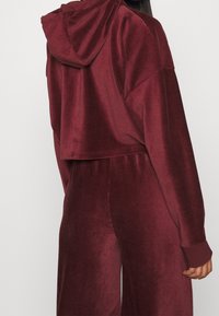 Bordeaux geknipte hoodie van een zachte, gestructureerde stof en met een capuchon. Bevat ribgebreide boorden en heeft een relaxte pasvorm. Gepaard met bijpassende joggers.