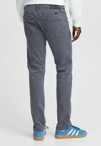 Vaqueros de mezclilla grises con cinco bolsillos, detalles de costura sutil y corte recto, llevados con zapatillas azules.