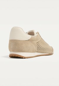 Sneaker beige en daim et cuir avec un design perforé, un dos texturé et une semelle contrastante. Profil bas, ajustement rembourré.