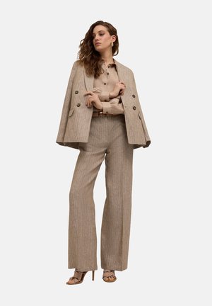 Beige gestreepte blazer met dubbele knopen, gecombineerd met een lichtbeige blouse en bijpassende brede broek. Hakken sandalen.