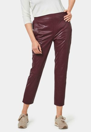 Burgundy leather trousers with a tailored fit, cropped length, and side pockets. Paired with light beige sneakers. Smooth texture.