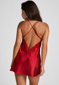 Vestido de satén rojo tipo slip con detalles de encaje, tirantes ajustables en forma de cruz y diseño sin espalda. Textura suave y acabado con ligero brillo.