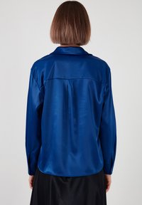 Blue satin shirt with a smooth texture, long sleeves, and a collar. Features a back yoke and a curved hem. Simple, solid color design.