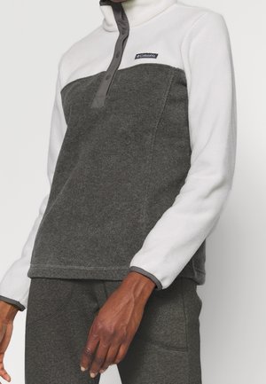 Person trägt einen grau-weißen Columbia Fleece-Pullover mit Druckknöpfen, kombiniert mit passenden grauen Hosen vor einfarbigem Hintergrund.