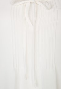 Blusa bianca con pieghe verticali e scollo a cravatta. Il tessuto appare liscio con una consistenza morbida e un design leggero.
