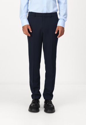 Die marineblauen Anzughosen zeichnen sich durch ein gerades Beinendes Design, glattes Material und einen dezenten Bügel aus. Sie werden mit einem hellblauen Hemd und schwarzen Schuhen getragen.