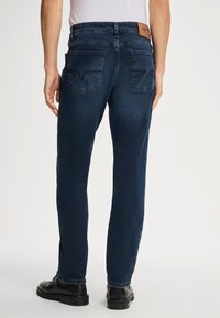 Jeans in denim blu scuro con vestibilità slim, dotati di due tasche posteriori con una sottile cucitura a forma di V e un'etichetta in pelle sul girovita.