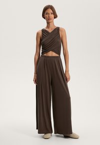 Braunes zweiteiliges Outfit mit einem ärmellosen, wendbaren Top und weit geschnittenen Hosen aus weichem, glattem Stoff.