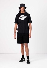 Svart kortermet t-skjorte med hvit "KINGS" grafikk, kombinert med svarte shorts og svarte joggesko. Bucket hat fullfører antrekket.