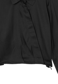 Chemise noire à manches longues avec un col, ourlet asymétrique, tissu texturé et détail de fermeture éclair sur le côté en bas.