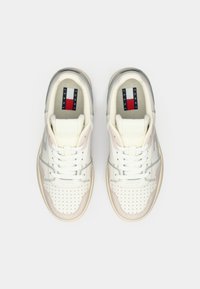 Para białych skórzanych sneakersów z beżowymi i szarymi akcentami, perforowany czubek, białe sznurówki oraz logo Tommy Jeans na wkładce.