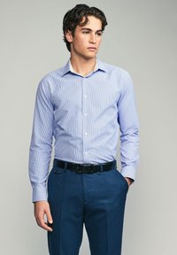 Chemise bleu clair à motifs avec un col boutonné, assortie à un pantalon bleu foncé et une ceinture noire. Tissu lisse et coupe ajustée.