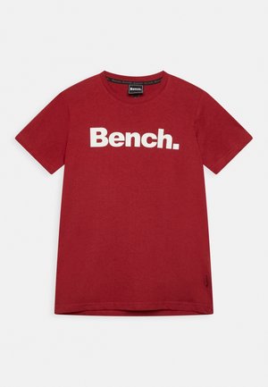 Camiseta roja de manga corta con texto blanco "Bench." impreso en el pecho, cuello redondo y una pequeña etiqueta de tela en el lado inferior.