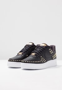 Sneakers in pelle nera con borchie a forma di stella dorata, suola in gomma bianca e lacci neri. Presentano una linguetta con accenti dorati e una zona delle punte traforata.