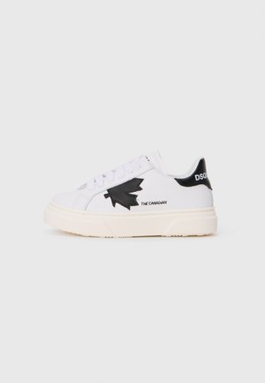 Witte sneaker met zwart esdoornblad logo en de tekst "THE CANADIAN." Voorzien van een getextureerde rubberen zool en een vetersluiting aan de voorkant met een zwarte hielaccent.