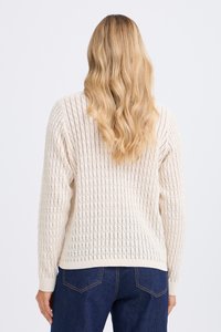 Pull en tricot couleur crème avec un design texturé en côtes, col rond et manches longues, associé à un jean en denim foncé.