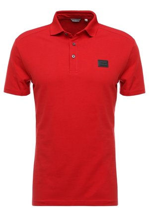 Czerwona koszulka polo z krótkim rękawem, zapinana na dwa guziki, z małą czarną prostokątną naszywką z logo na lewej piersi.