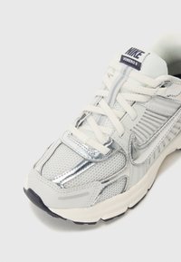Bijele Nike Vomero 5 tenisice s gornjištem od mreže, srebrnim detaljima, bijelim vezicama i crnom gumenom potplatom.