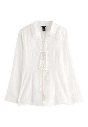 Hvid, langærmet bluse lavet af letvægtsstof, med blomsterblondekant, bindebånd ved halsen og en bølget kant. Dekoreret med broderede detaljer.