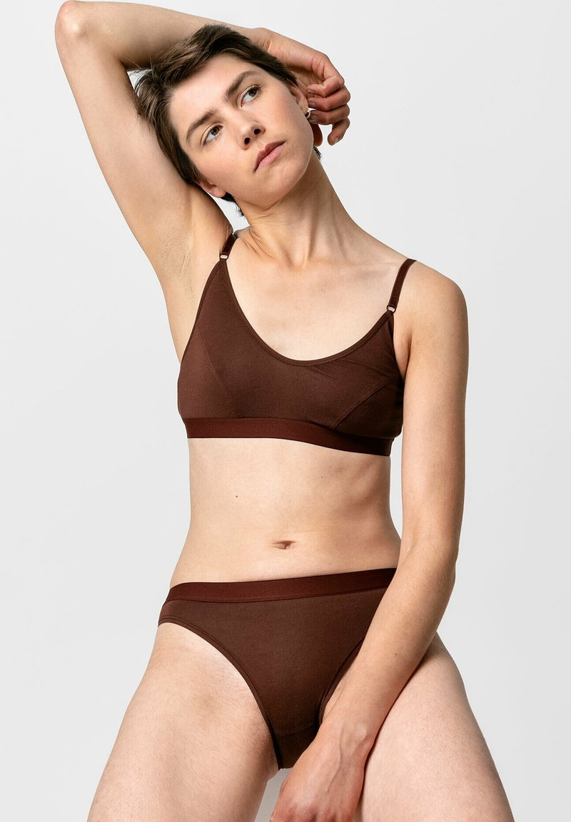 Bruine bralette en bijpassende slip gemaakt van een gladde, rekbare stof. Het ontwerp heeft dunne, verstelbare bandjes en gebande randen.