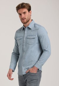 Lichtblauwe denim overhemden met een subtiele patroonstructuur, lange mouwen, drukknopen en twee voorzakken.