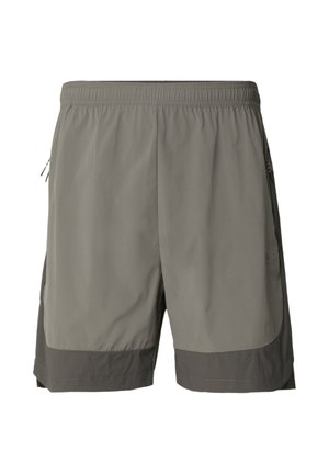 Mand iført grå sportsshorts med mørk kant, hvide sokker og hvide sneakers, står foran en ensfarvet lysegrå baggrund.